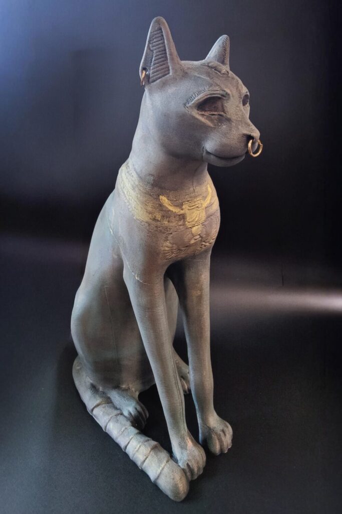 3D printed statue of a cat with gold rings in its ears and nose. It's been painted to mimic aged bronze.